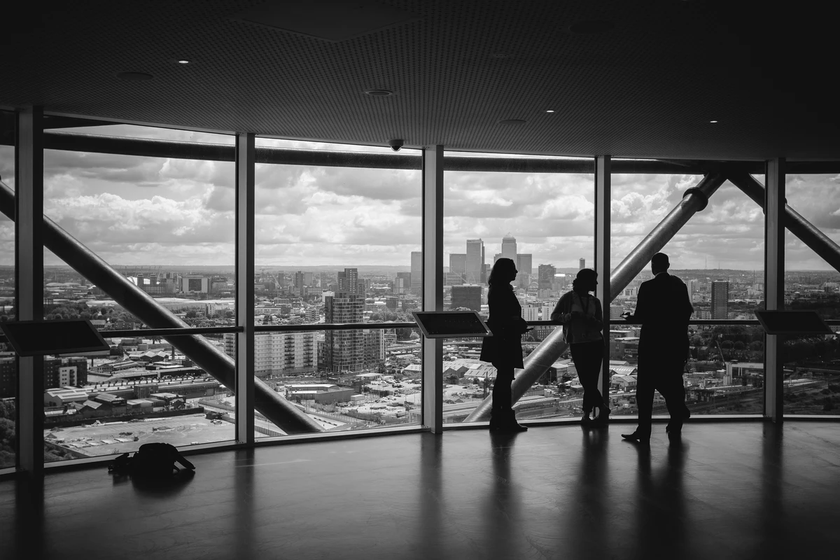 Three business people stood at a full length window looking over a city skyline